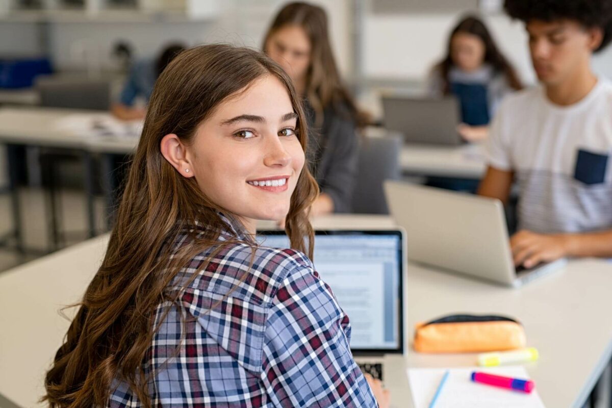 Smiling school girl in uniform working on laptop