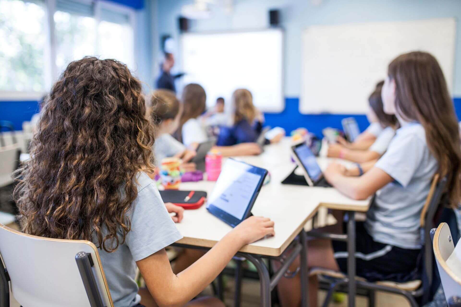 Classroom of students with tablets all looking at smartboard